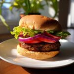 Zbliżenie na gotowy burger sojowy na białym talerzu, z sałatą, pomidorem i czerwoną cebulą.