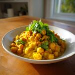 Miseczka pełna kremowej, żółtej ciecierzycy w curry, obficie udekorowana świeżą kolendrą.
