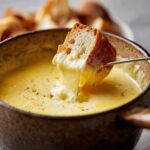 Kawałek chleba zanurzony w gorącym, ciągnącym się fondue serowym, posypanym pieprzem.