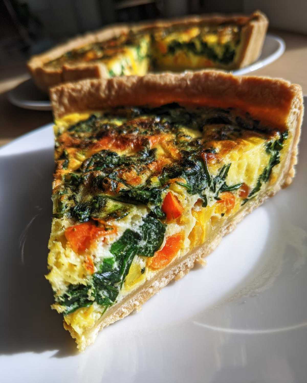 Zbliżenie na kawałek quiche z warzywami, widoczne szpinak i marchewka w jajecznej masie.