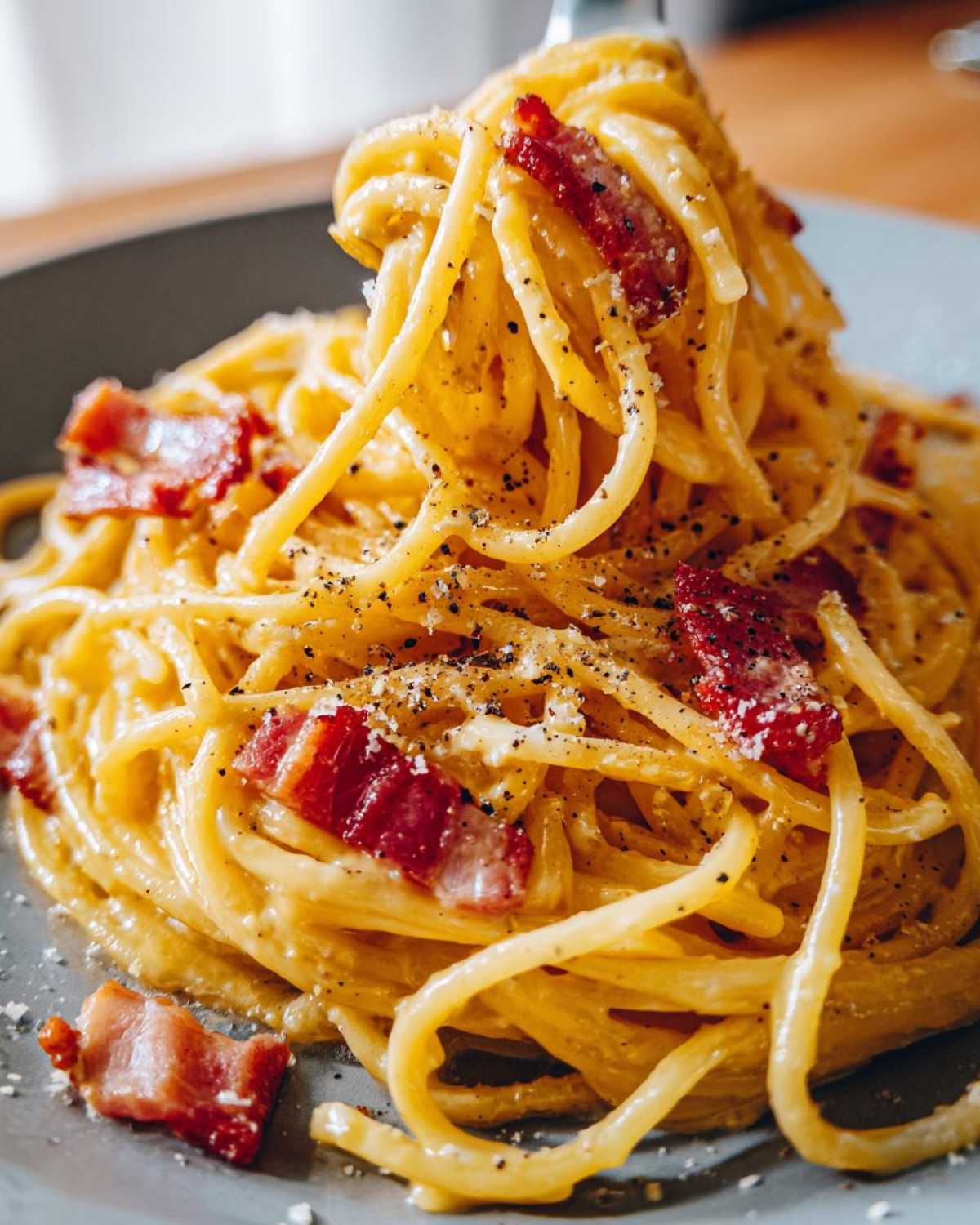 Zbliżenie na porcję kremowego spaghetti carbonara z kawałkami boczku i świeżo mielonym pieprzem.