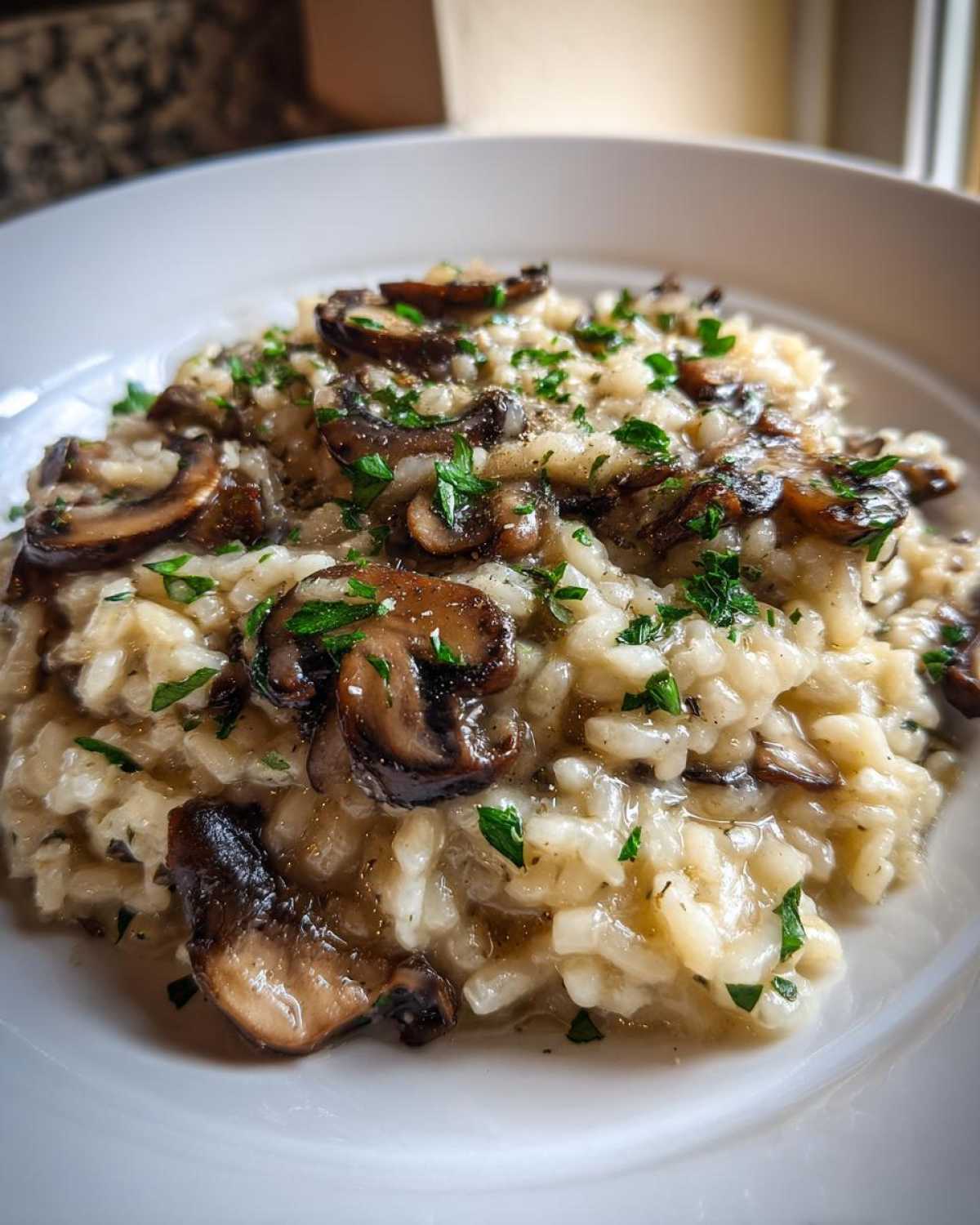 Zbliżenie na kremowe risotto grzybowe z kawałkami podsmażonych grzybów i posiekaną natką pietruszki.