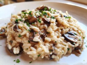 Zbliżenie na kremowe risotto grzybowe posypane świeżą, posiekaną natką pietruszki na białym talerzu.