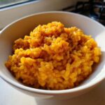 Zbliżenie na kremowe, pomarańczowe risotto z dyni posypane przyprawami w białej misce.