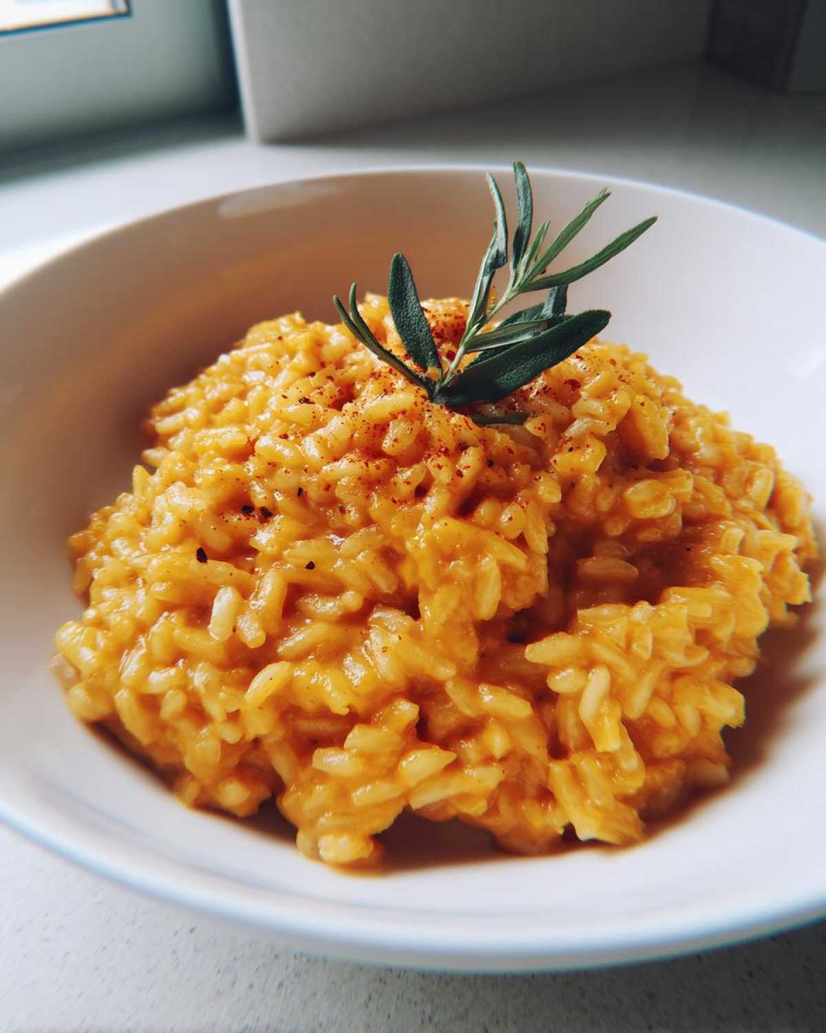Zbliżenie na kremowe risotto z dyni w białej misce, udekorowane świeżą gałązką rozmarynu.