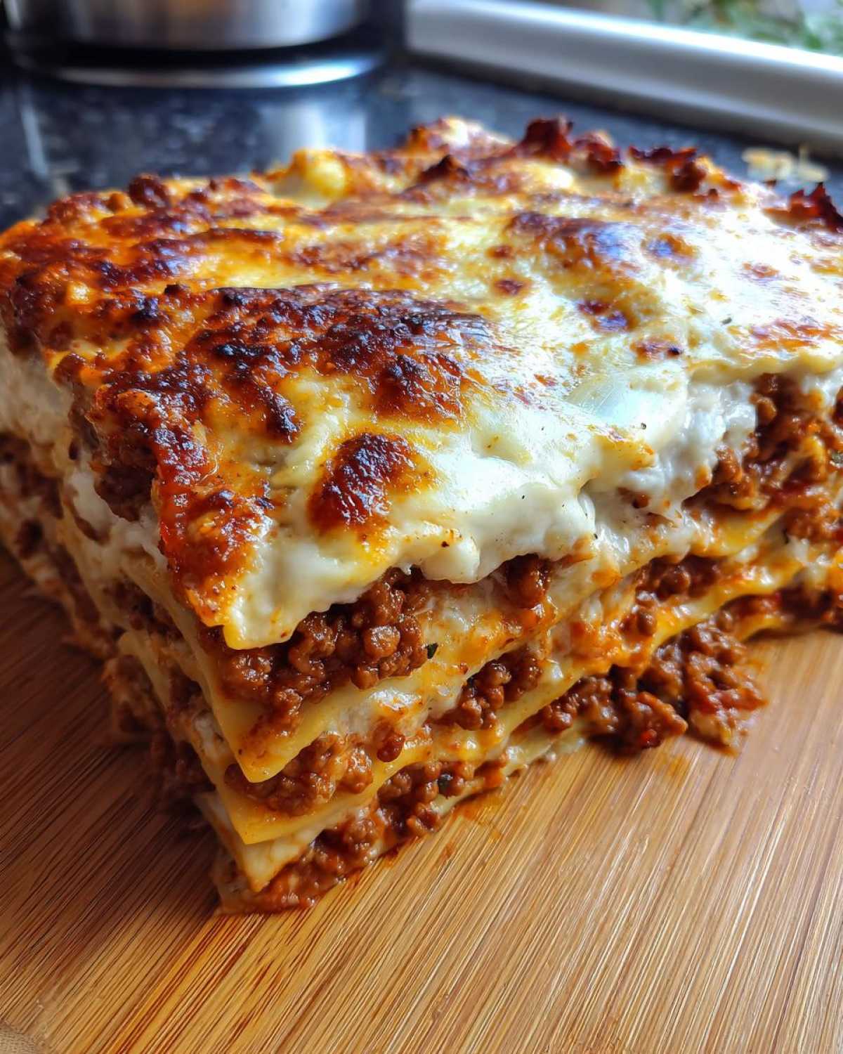 Kawałek lasagne z mięsem mielonym na desce, z widocznymi warstwami makaronu, sosu mięsnego i sera.
