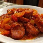 Zbliżenie na porcję leczo węgierskiego z grubymi plastrami kiełbasy i kawałkami papryki w intensywnym, czerwonym sosie.