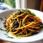 Zbliżenie na talerz z makaronem pasta puttanesca, obficie posypanym oliwkami i natką pietruszki.