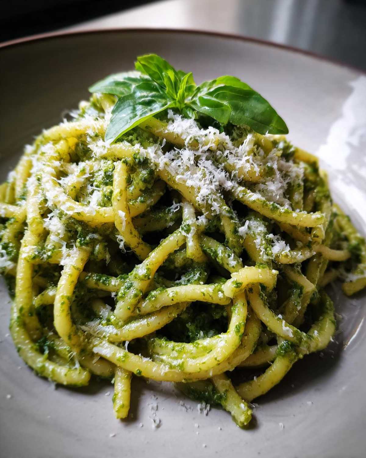 Zbliżenie na talerz z makaronem z pesto, posypany parmezanem i udekorowany listkami bazylii.