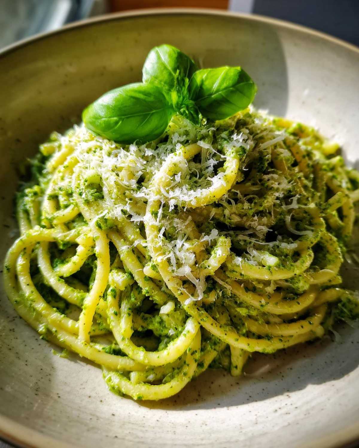 Zbliżenie na talerz makaronu z pesto, posypanego parmezanem i udekorowanego listkami bazylii.