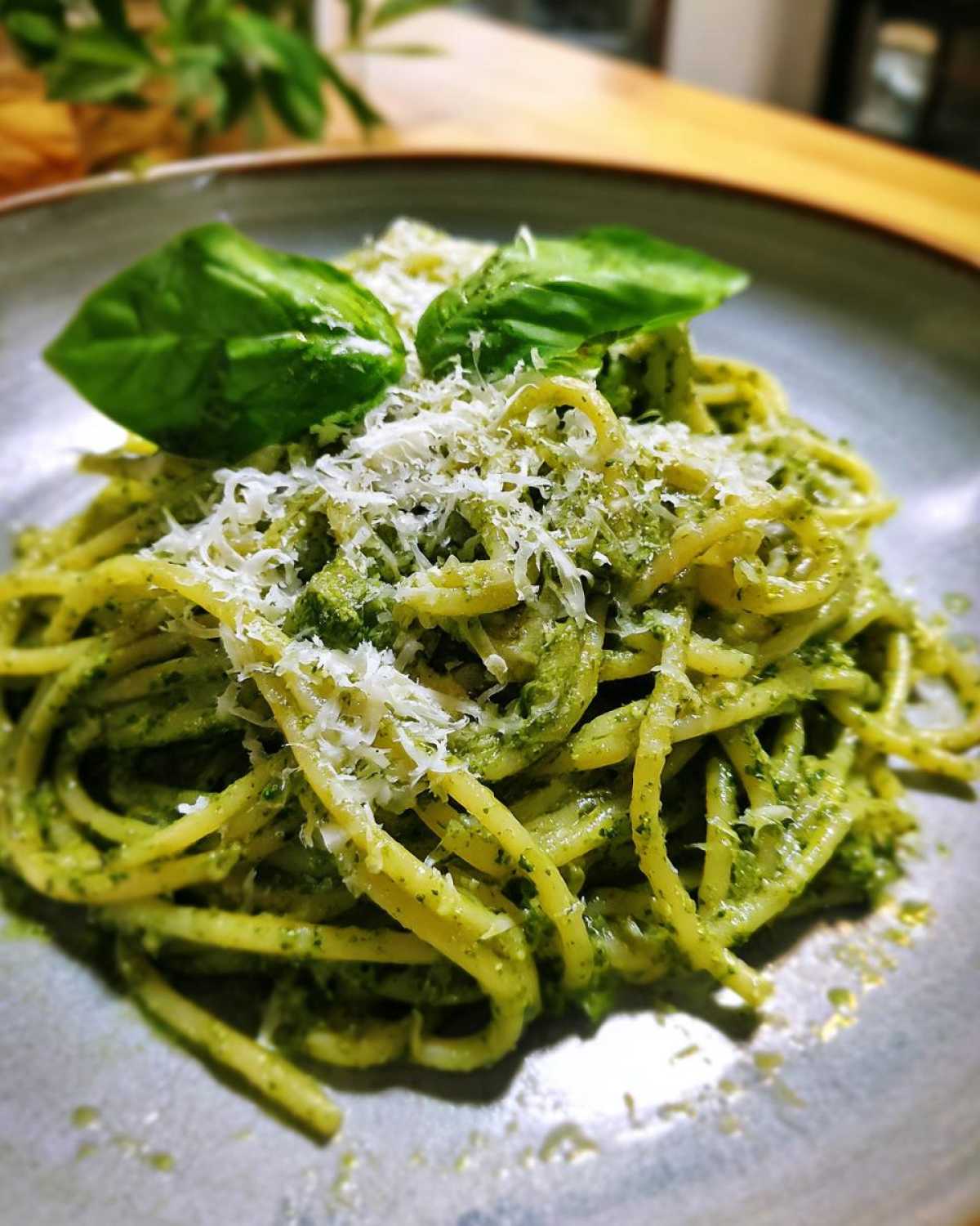 Talerz pełen makaronu z pesto, posypany parmezanem i udekorowany listkami bazylii.