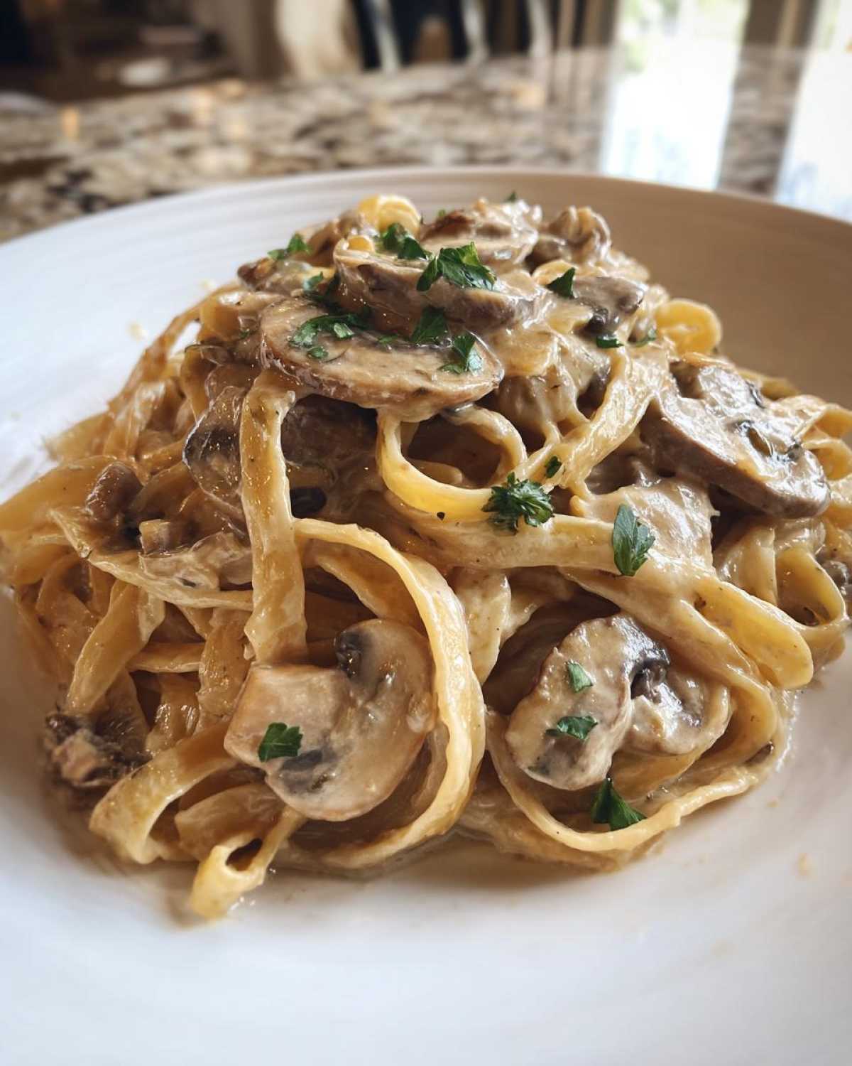Zbliżenie na talerz z makaronem tagliatelle polanym gęstym, kremowym sosem grzybowym i posypany natką pietruszki.