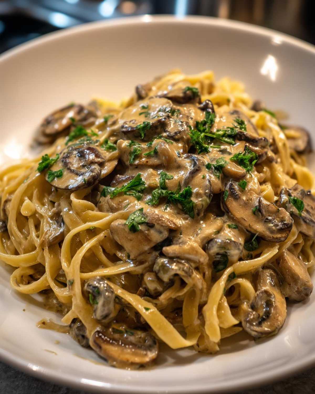 Zbliżenie na talerz pełen makaronu tagliatelle polanego kremowym sosem grzybowym i posypanego natką pietruszki. Idealny makaron z sosem grzybowym.