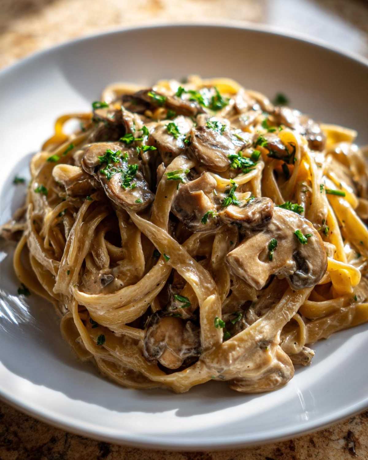 Zbliżenie na talerz pełen makaronu tagliatelle z kremowym sosem grzybowym i posiekaną natką pietruszki.