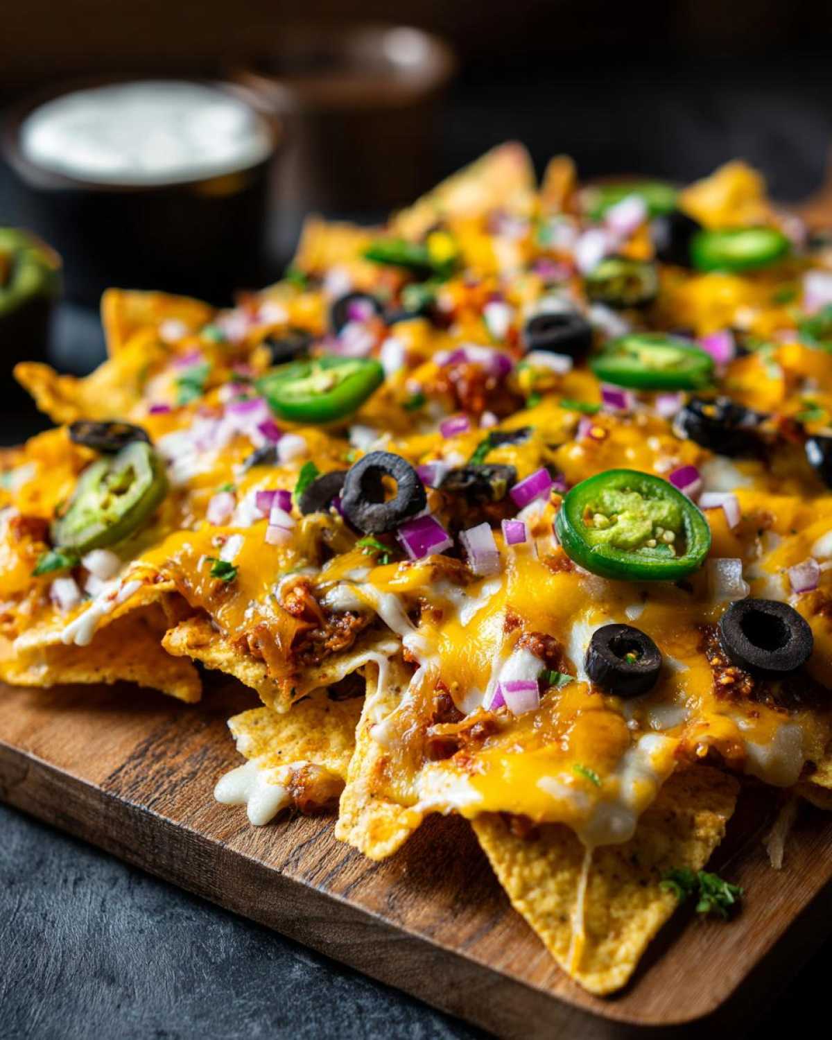 Zbliżenie na talerz nachos zapiekanych z serem, jalapeno, oliwkami i cebulą.
