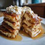 Zbliżenie na stos puszystych pancakes z twarogiem, polane syropem klonowym, przekrojone na pół.