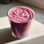 Zbliżenie na gęsty, różowo-fioletowy shake jagodowy z pianką na wierzchu, stojący w szklance.