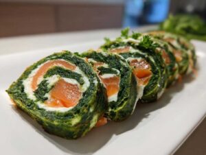 Pokrojona rolada szpinakowa z łososiem i kremowym serkiem, udekorowana natką pietruszki.