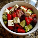 Zbliżenie na miskę pełną świeżej sałatki greckiej z serem feta, pomidorami, ogórkiem i oliwkami.