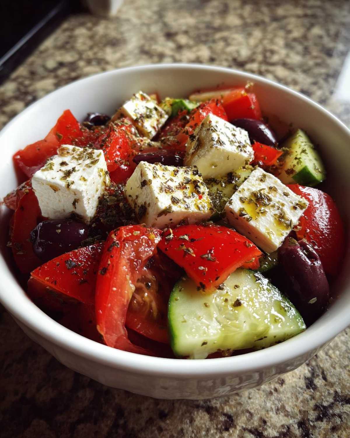Zbliżenie na miskę pełną świeżej sałatki greckiej z serem feta, pomidorami, ogórkiem i oliwkami.