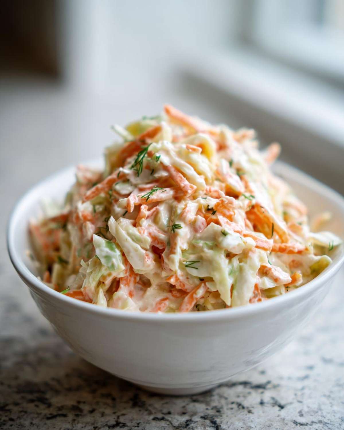 Miseczka kremowej surówki coleslaw z posiekaną kapustą i marchewką, udekorowana koperkiem.