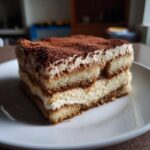 Kawałek pysznego tiramisu na białym talerzu, posypany kakao.