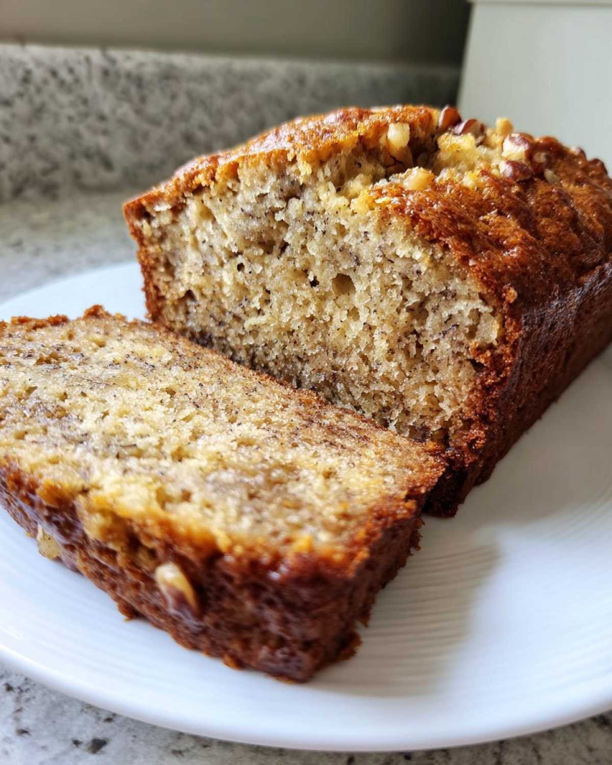 Przekrój wilgotnego ciasta bananowego z widocznymi kawałkami banana i orzechami na wierzchu.