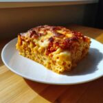 Kawałek zapiekanka makaronowa z serem na białym talerzu, z chrupiącą, zapieczoną skórką serową.