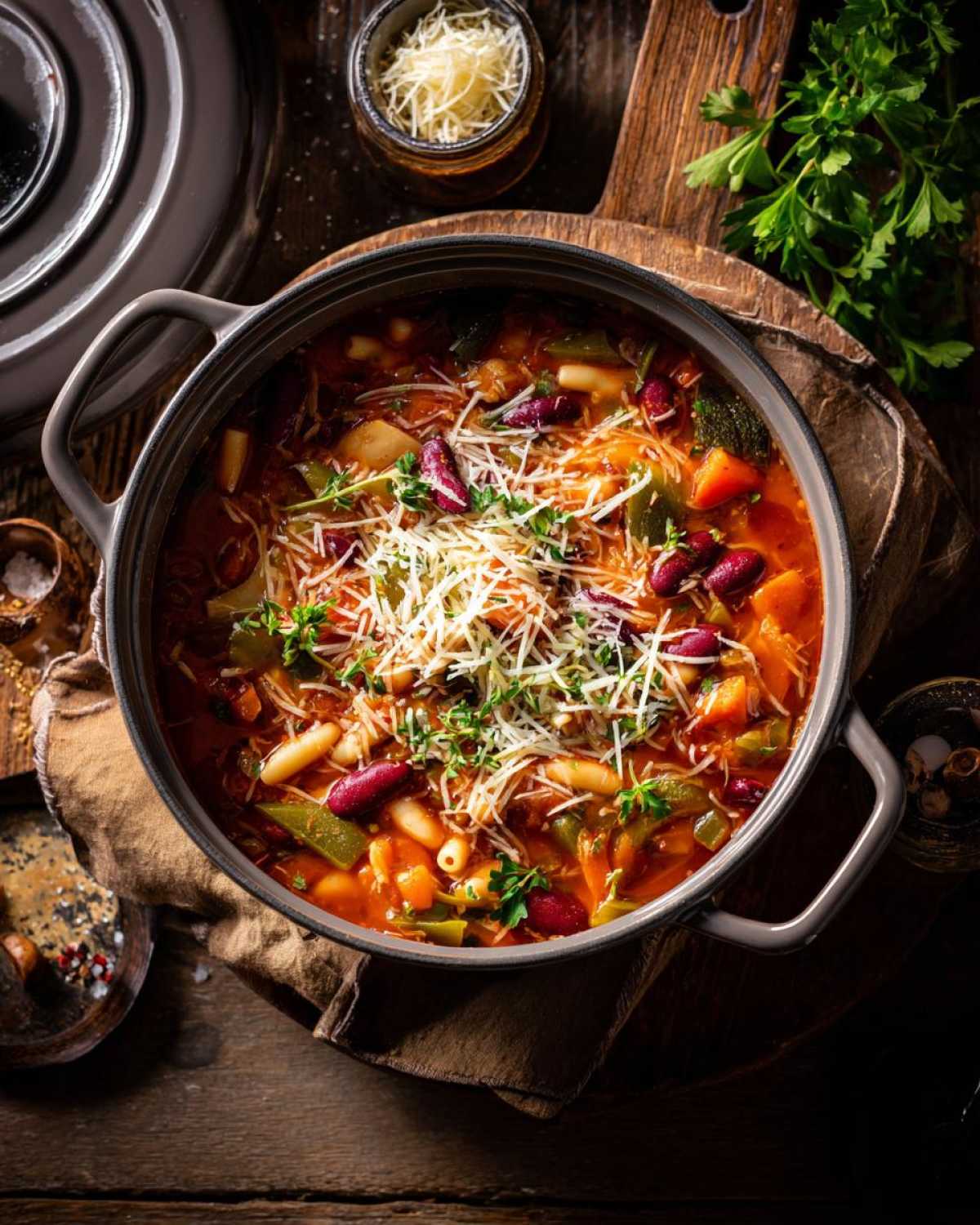 Górny widok na garnek pełen aromatycznej zupy minestrone z widocznymi fasolą, makaronem, marchewką i innymi warzywami, posypanej tartym serem.