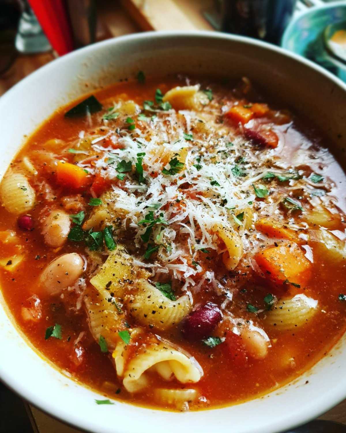Zbliżenie na miskę zupy minestrone z makaronem, fasolą, marchewką i posypką z parmezanu.
