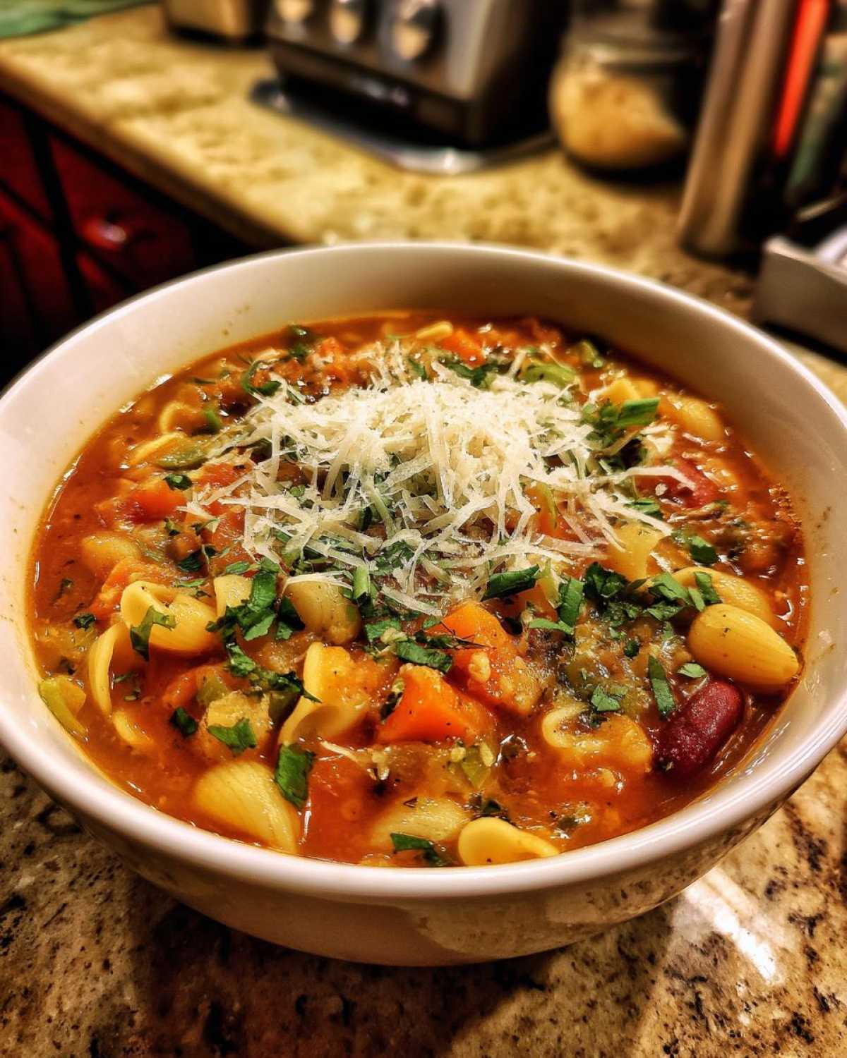 Miseczka pełna aromatycznej zupy minestrone z makaronem, fasolą, warzywami i posypką z parmezanu.