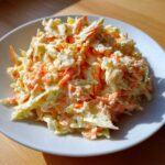Zbliżenie na kremową Sałatka coleslaw z tartą marchewką i kapustą, podana na białym talerzu.