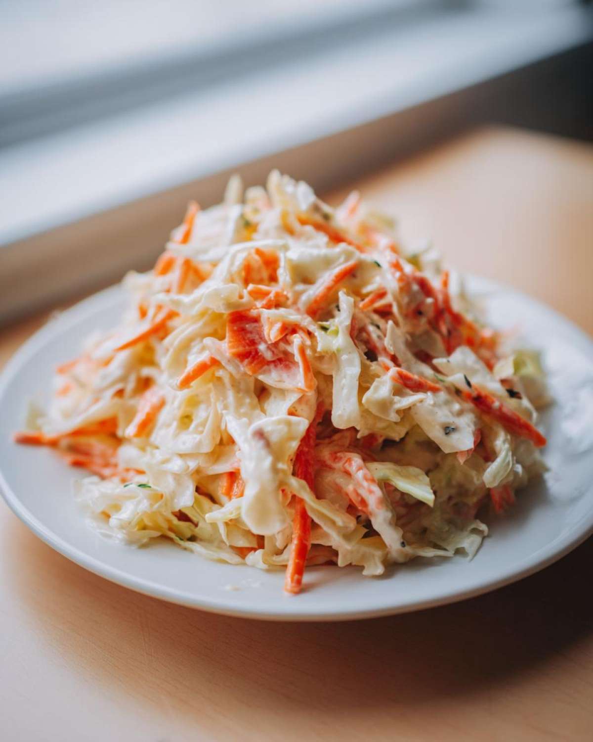 Zbliżenie na kremową Sałatka coleslaw z tartą marchewką i kapustą na białym talerzu.