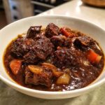 Zbliżenie na miskę pełną aromatycznego gulaszu wieprzowego z kawałkami mięsa, marchewką i cebulą w ciemnym sosie.