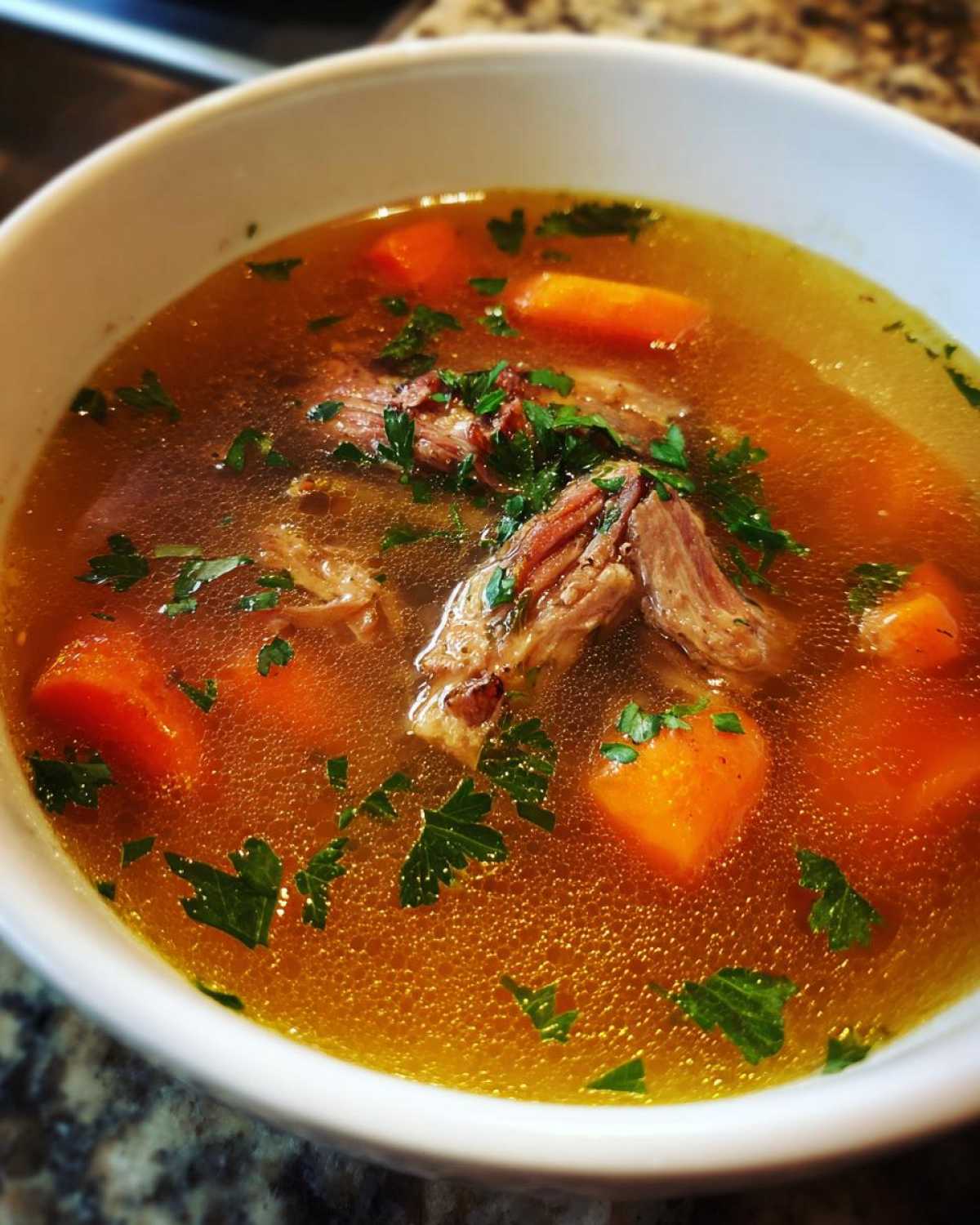 Zbliżenie na miskę aromatycznego Rosół z kaczki z kawałkami mięsa, marchewką i natką pietruszki.