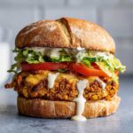 Zbliżenie na soczysty Burger z ciecierzycy z roztopionym serem, pomidorem, sałatą i białym sosem.