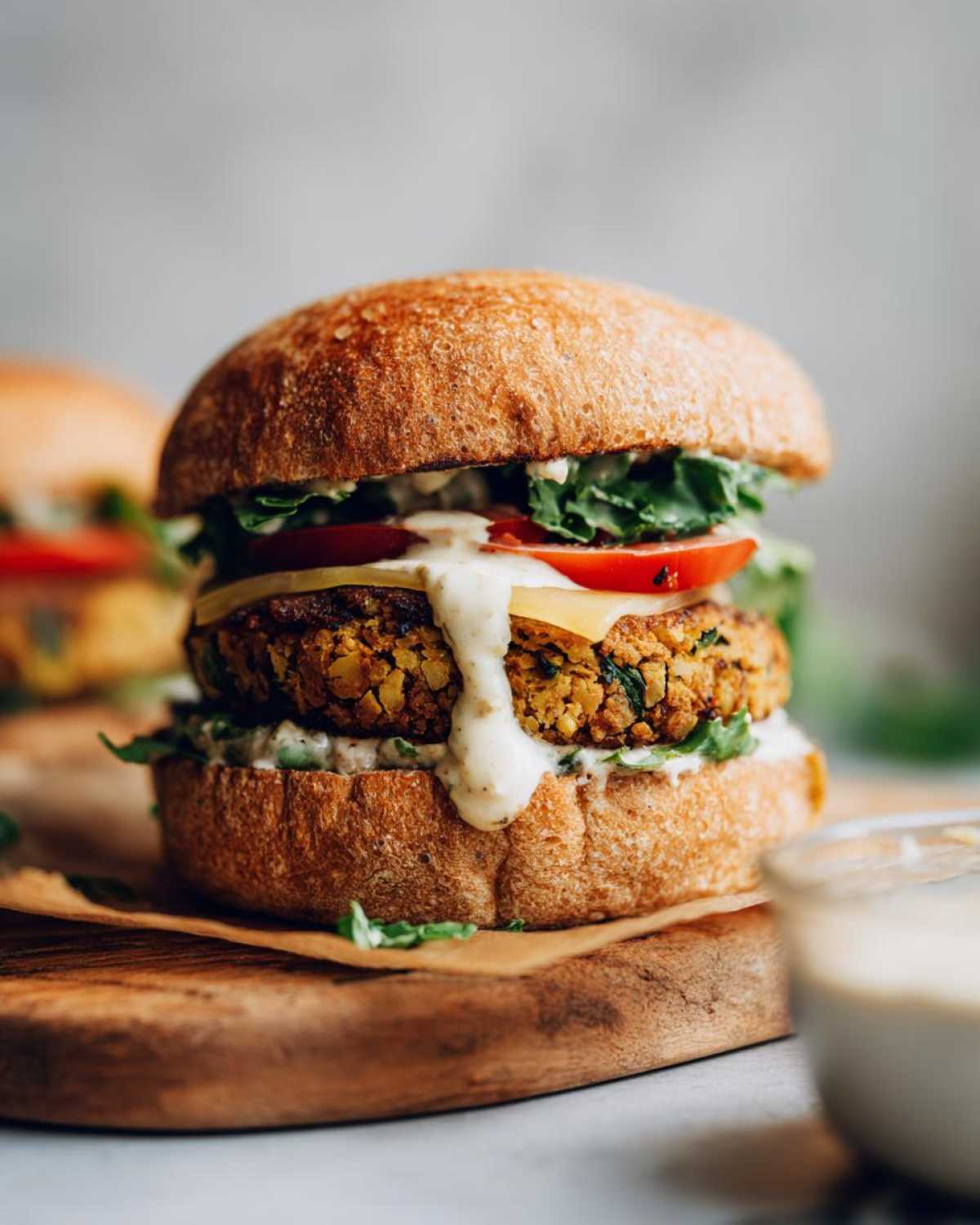 Zbliżenie na apetyczny Burger z ciecierzycy w bułce z sosem, serem i pomidorem.