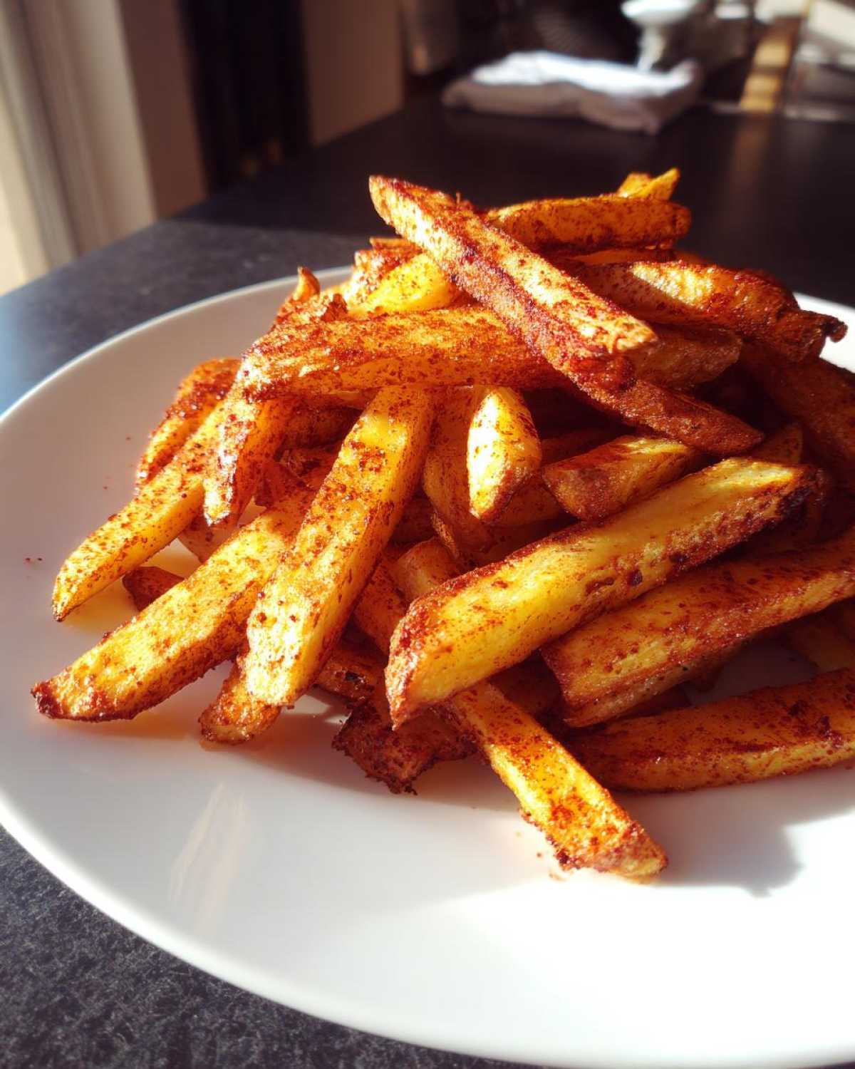 Stos chrupiących, przyprawionych Frytki z piekarnika podane na białym talerzu, oświetlone słońcem.