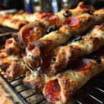 Zbliżenie na stos chrupiących paluchów pizzowych z serem, pepperoni i oliwkami, leżących na kratce chłodzącej.