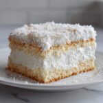 Przekrój Ciasta Raffaello z grubą warstwą białego kremu i wiórkami kokosowymi na wierzchu.