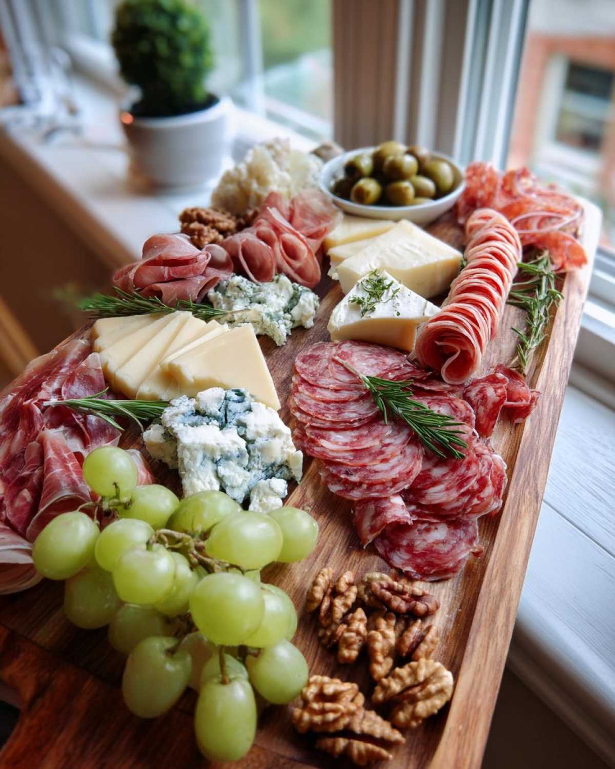 Zbliżenie na bogato udekorowaną deskę serów i wędlin, z serem pleśniowym, salami, winogronami i orzechami.