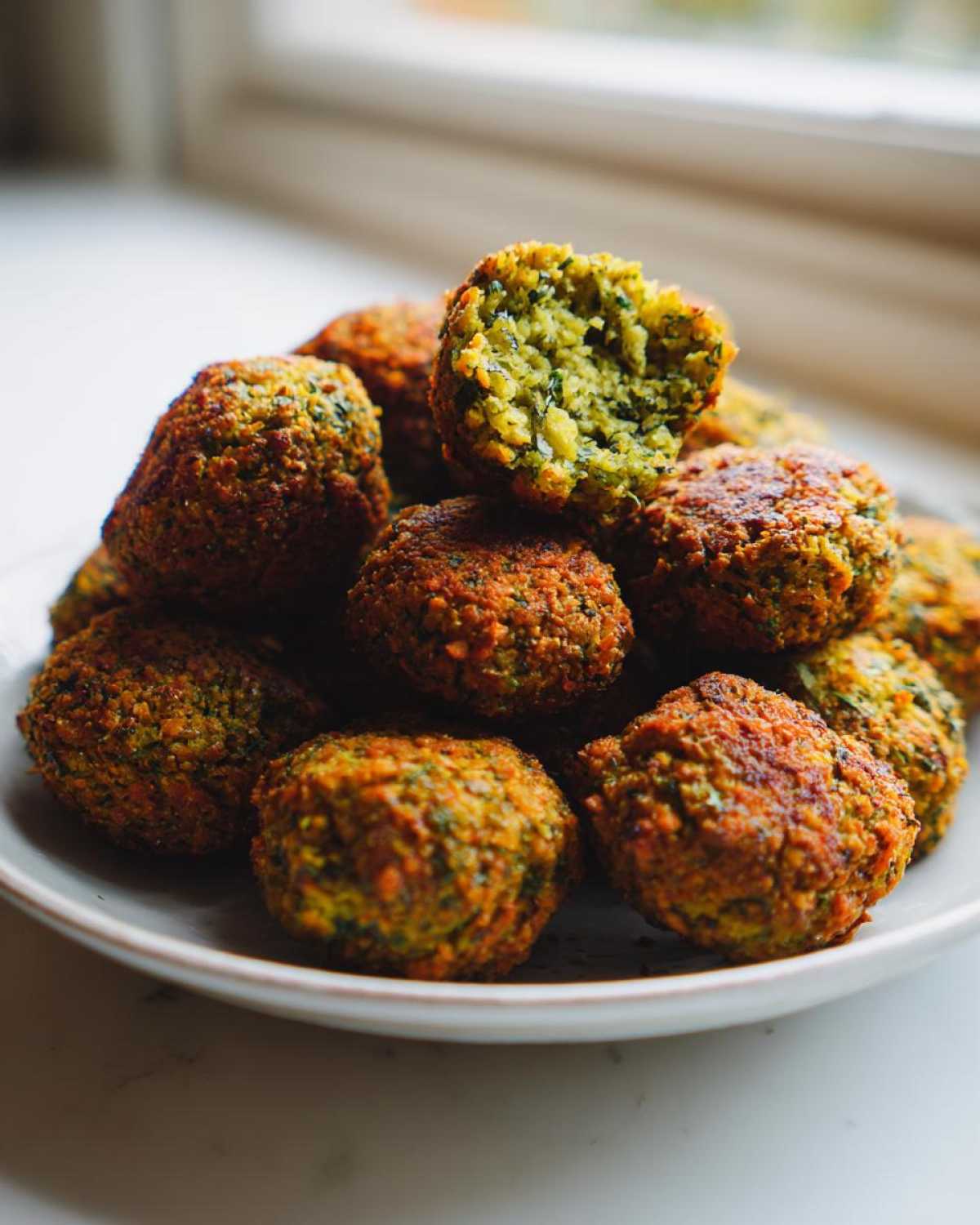 Stos domowych falafeli z ciecierzycy na talerzu, jeden przekrojony ukazuje zielone wnętrze.