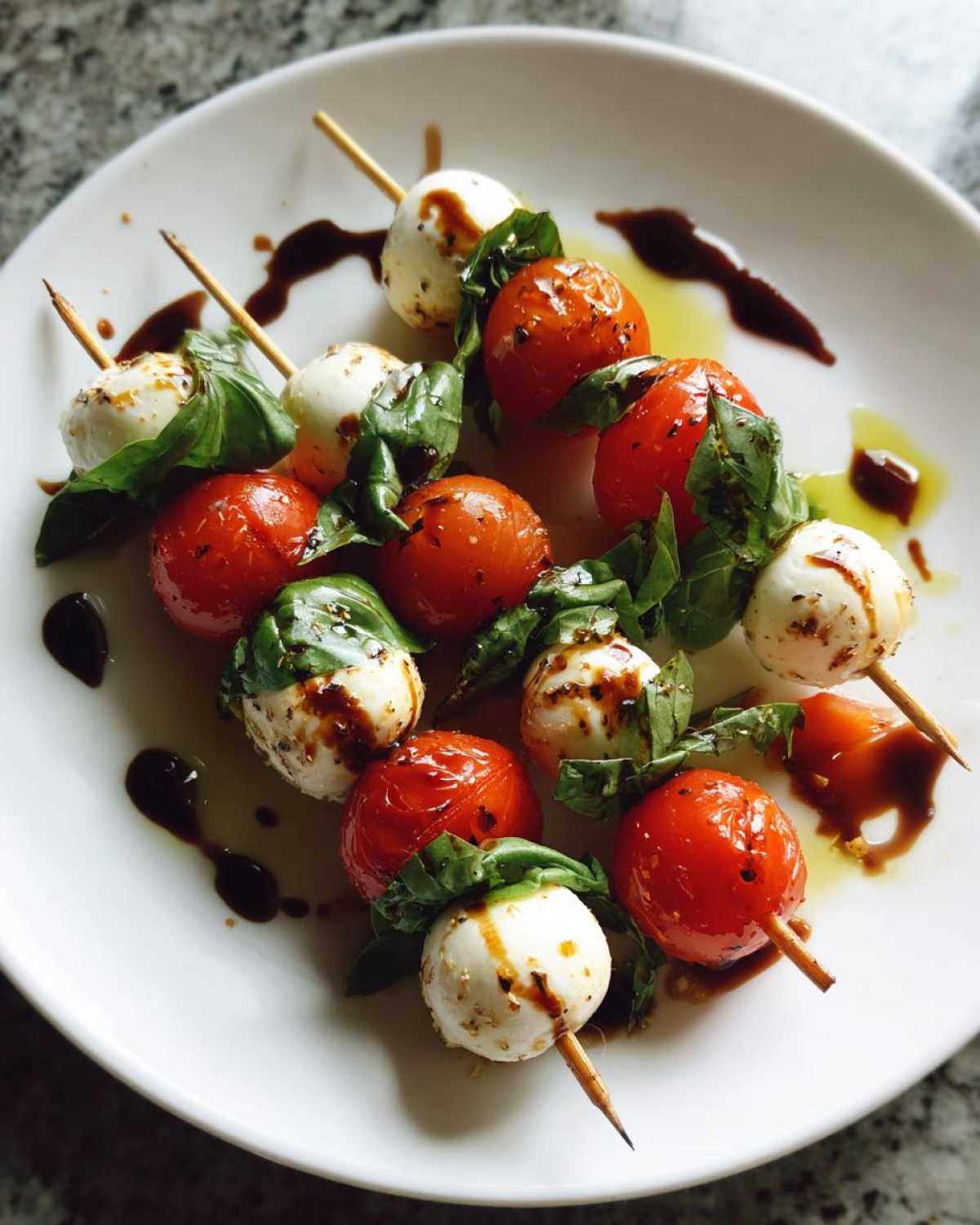 Zbliżenie na szaszłyki caprese z małymi kulkami mozzarelli, pomidorkami koktajlowymi i bazylią, polane sosem balsamicznym.