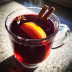 Zbliżenie na gorące Grzane wino z przyprawami, udekorowane laskami cynamonu, anyżem i plastrem pomarańczy.
