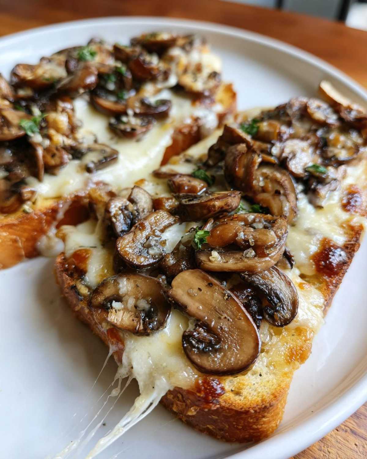 Dwie złociste grzanki z serem i dużą ilością podsmażanych pieczarek, ser ciągnie się apetycznie.