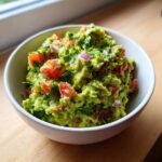 Zbliżenie na miskę pełną świeżego, zielonego Guacamole klasyczne z kawałkami pomidora i czerwonej cebuli.