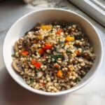 Zbliżenie na miskę pełną kaszy gryczanej z warzywami, w tym pieczarkami i papryką.