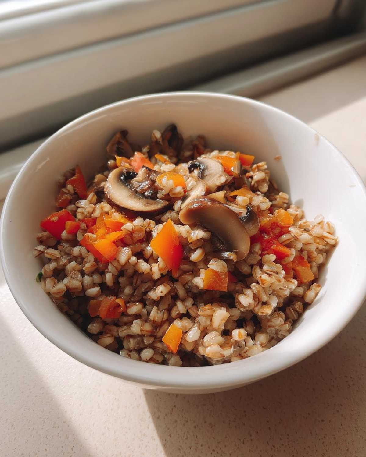 Zbliżenie na białą miseczkę pełną kaszy gryczanej z warzywami, w tym kawałkami pomidora i pieczarkami.