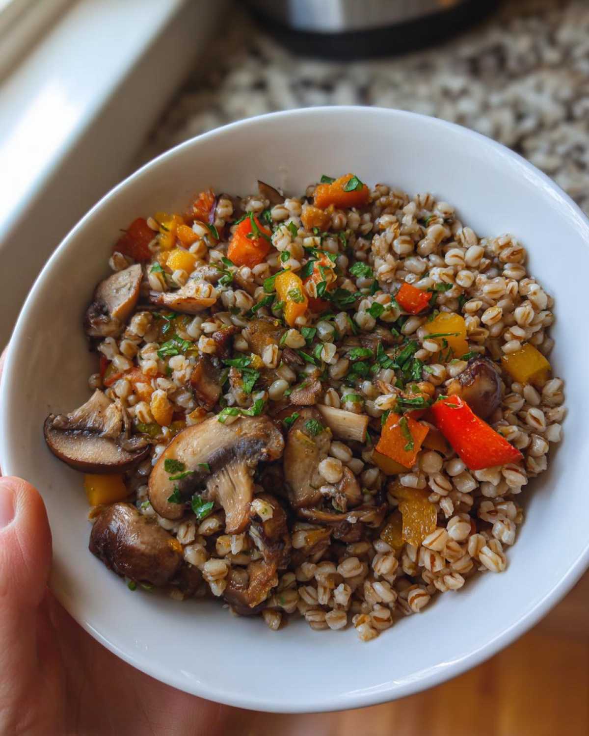 Zbliżenie na białą miseczkę wypełnioną kaszą gryczaną z warzywami, pieczarkami i posiekaną natką pietruszki.