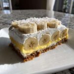 Przekrój ciasta Bananowa chmurka z warstwą spodu, kremu budyniowego, bitej śmietany i plasterkami banana.